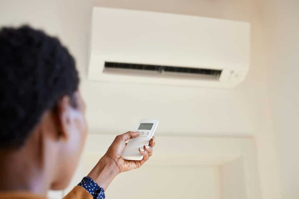 African american woman holding remote control aimed at air conditioner