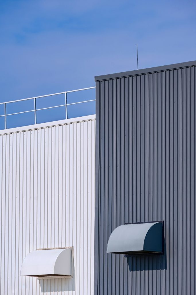 Air ducts ventilation on grey and white corrugated metal factory building wall against blue sky