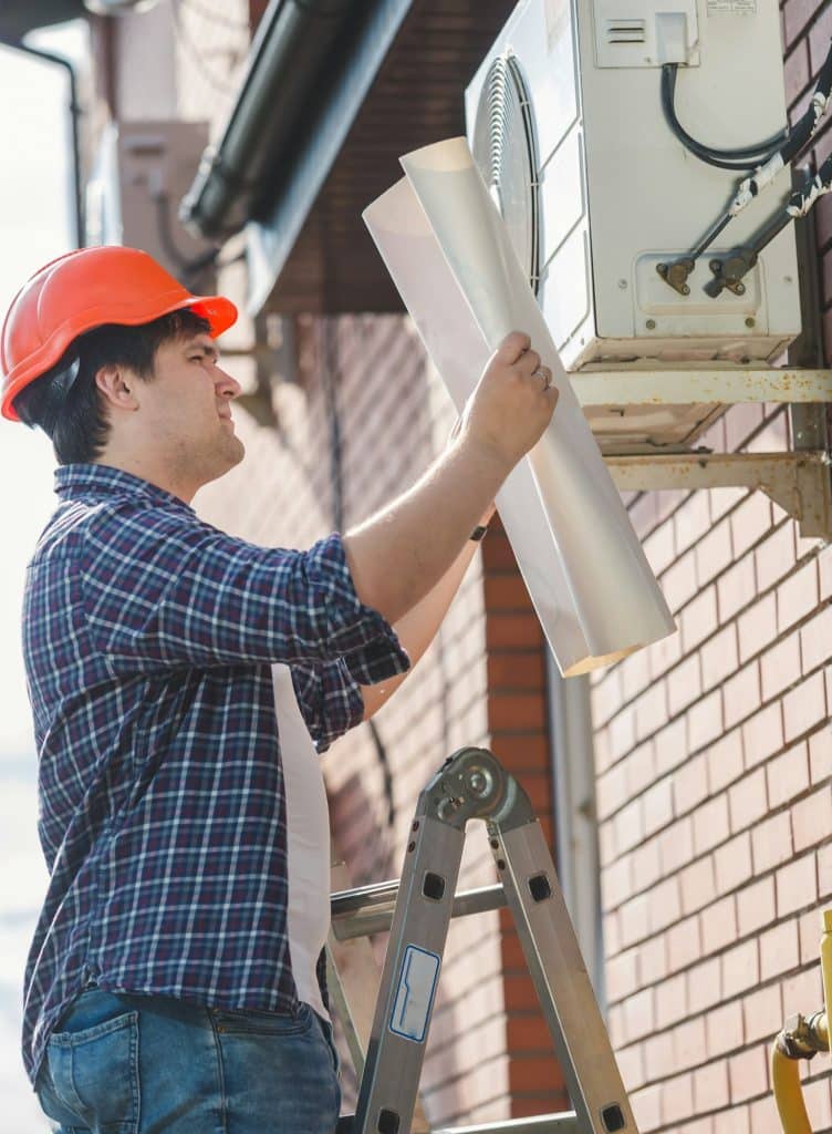 Engineer in hardhat looking in plan of air conditioning system