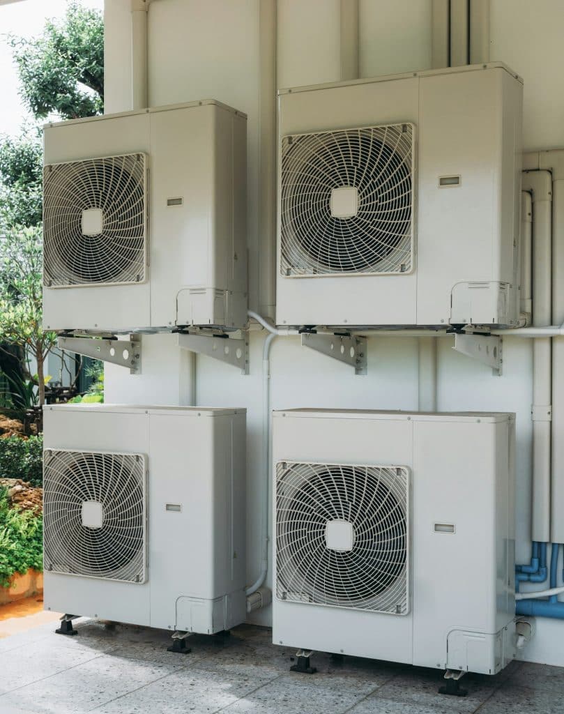 Four white air conditioners are mounted on a wall