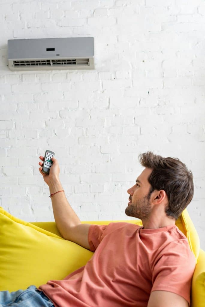 handsome young man holding remote control while lying on sofa under air conditioner