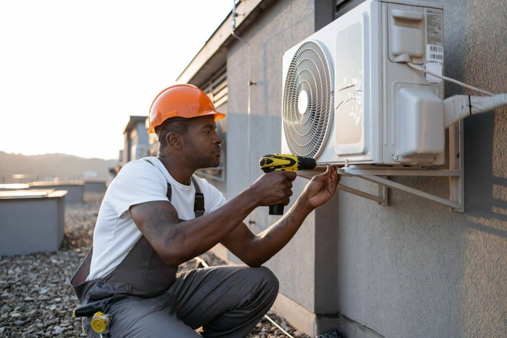 Man kneeling with screwdriver near air conditioner outdoors